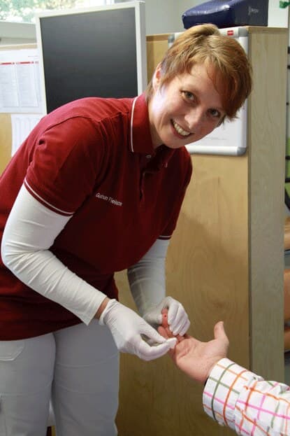 Eine medizinische Fachangestellte der Praxis nimmt einer Patientin Blut an der Fingerkuppe ab.